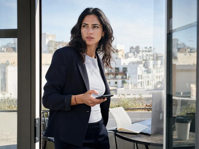 Femme en blazer utilisant smartphone sur terrasse urbaine